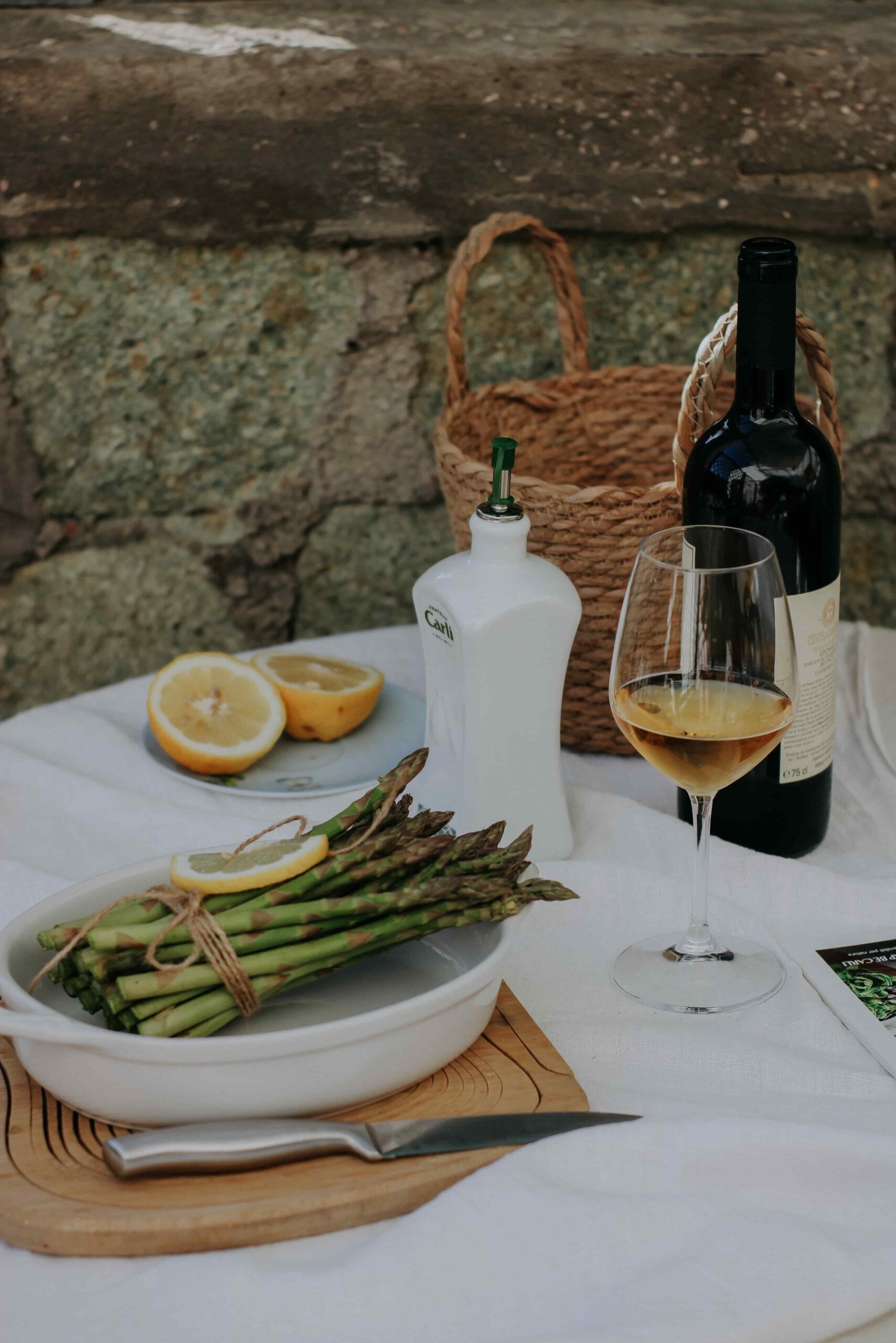 A dining table with asparagus, lemons, and orange wine on it