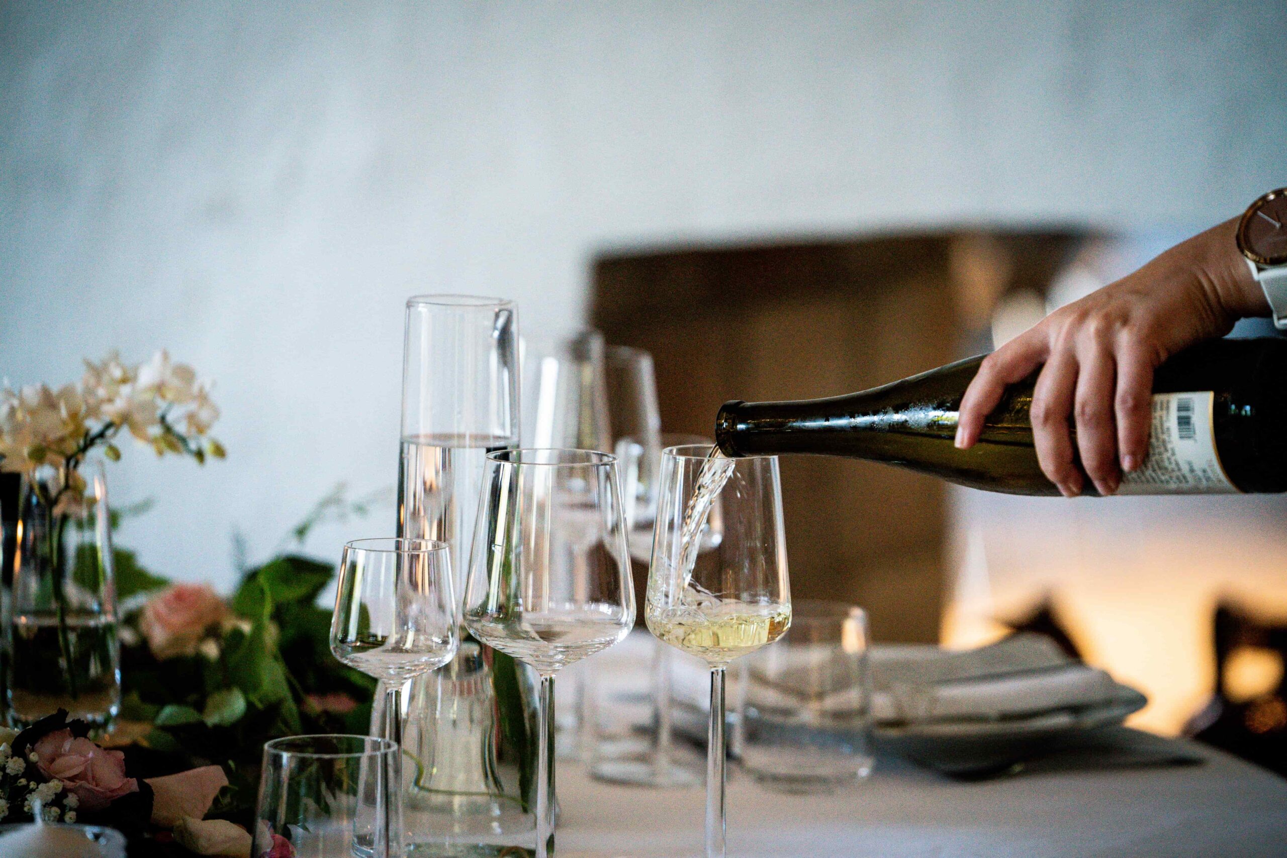A waiter pouring a glass of white wine at a restaurant dining table