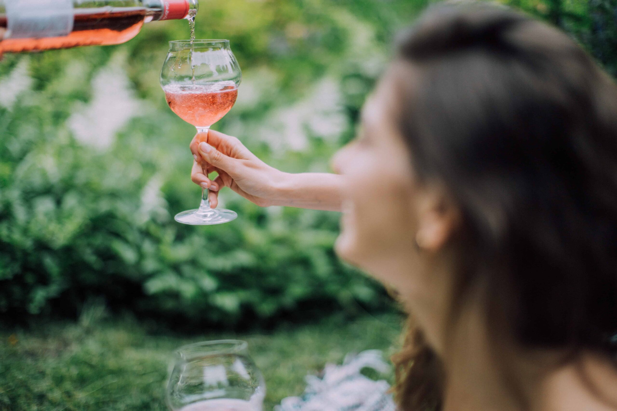 A person pouring a glass of wine for a friend who looks up at them