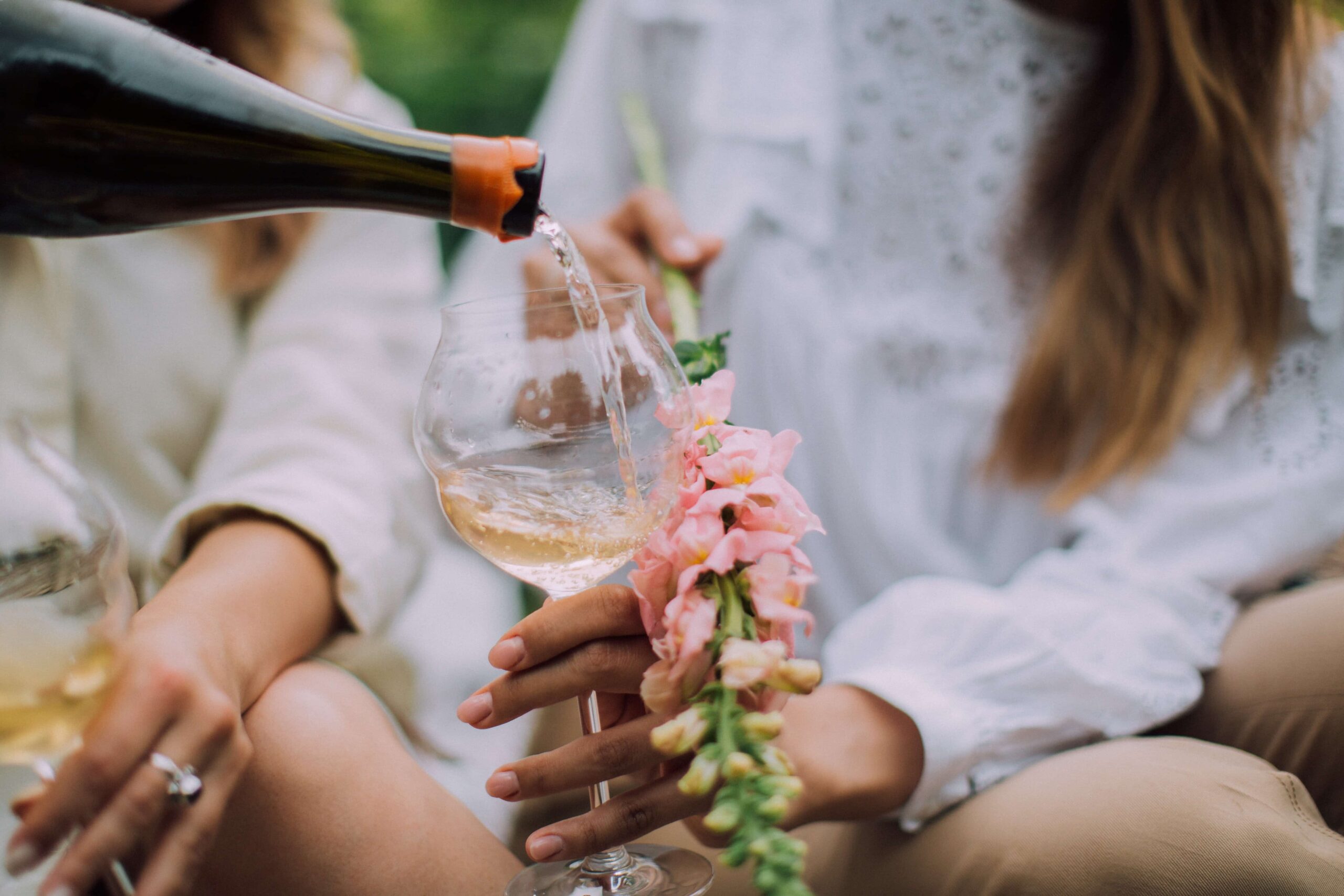 A woman holding flowers and a glass while someone pours her wine.