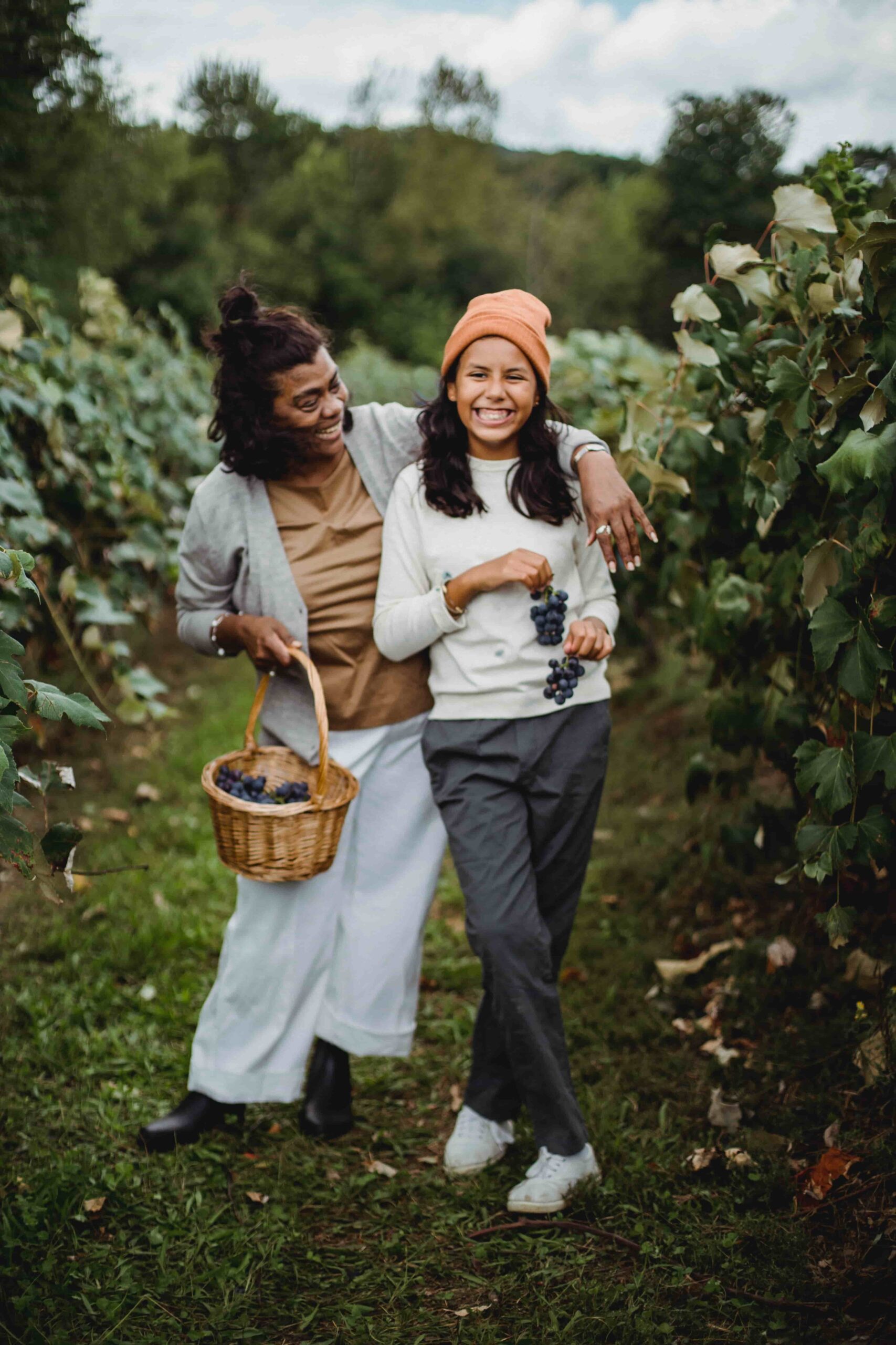 Two people smiling and holding grapes in a vineyard