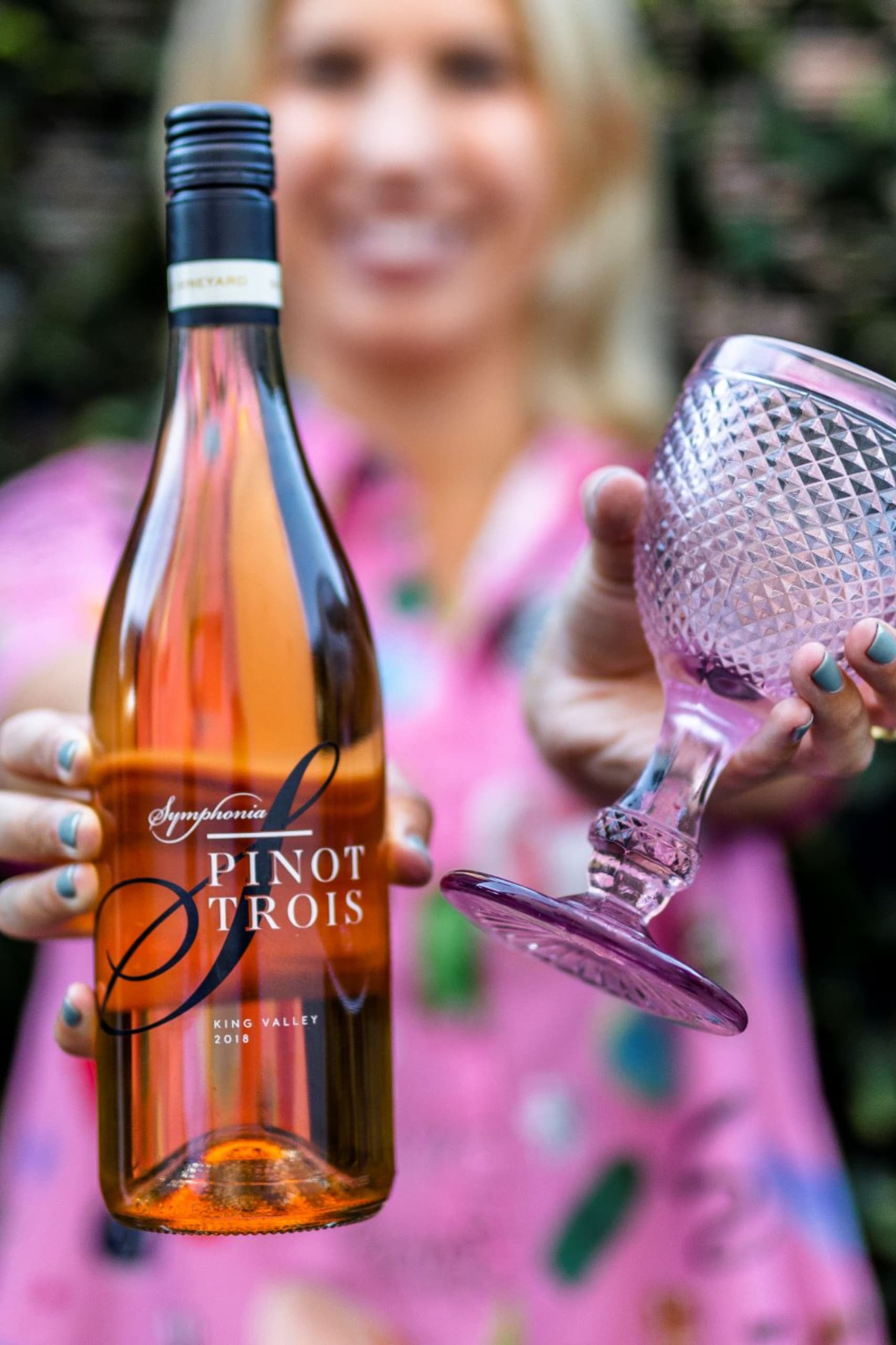 A woman holding a bottle of Pinot Trois from Symphonia Wines